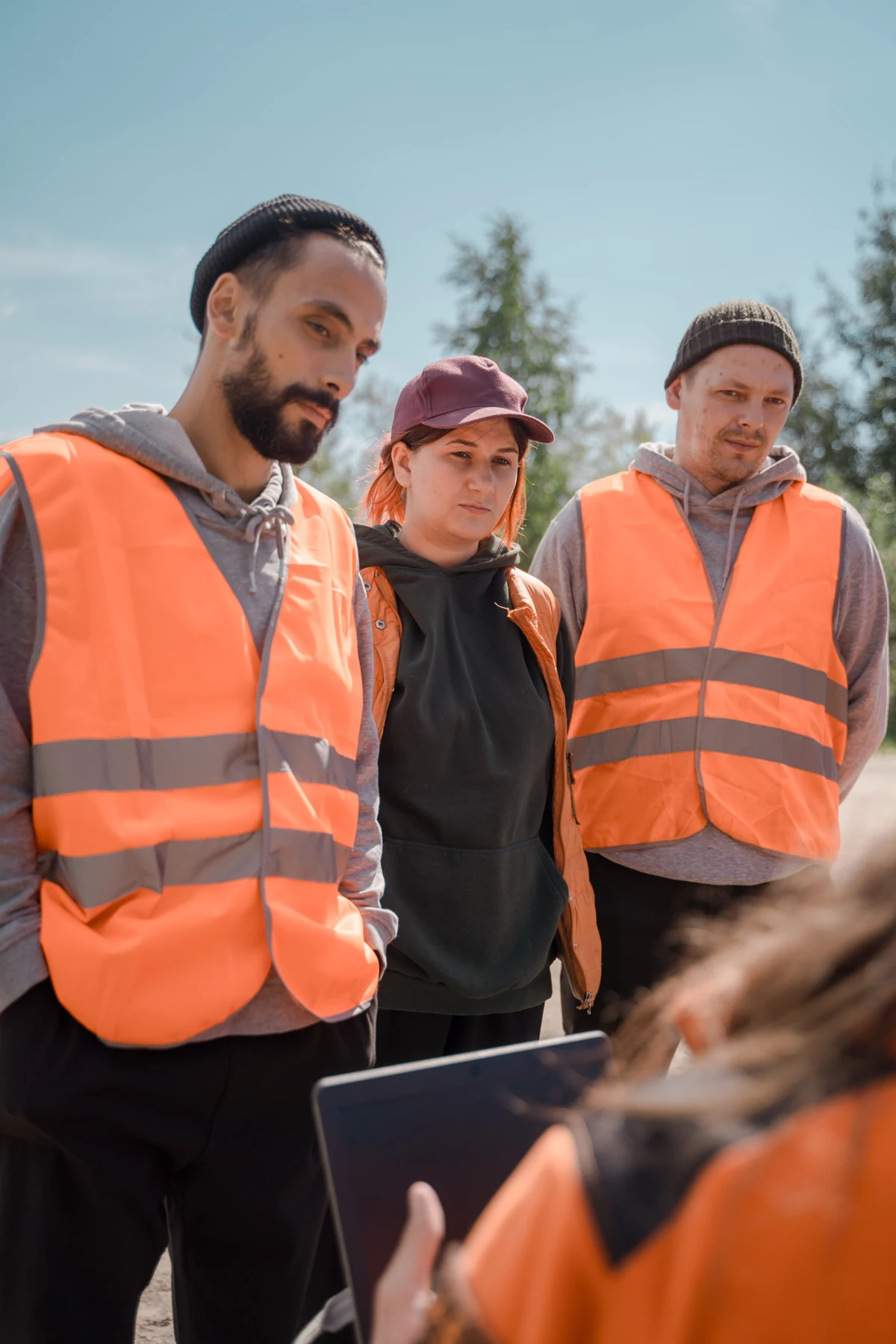 A group in high-visibility vests listening to an outdoor briefing, with the speaker in the foreground