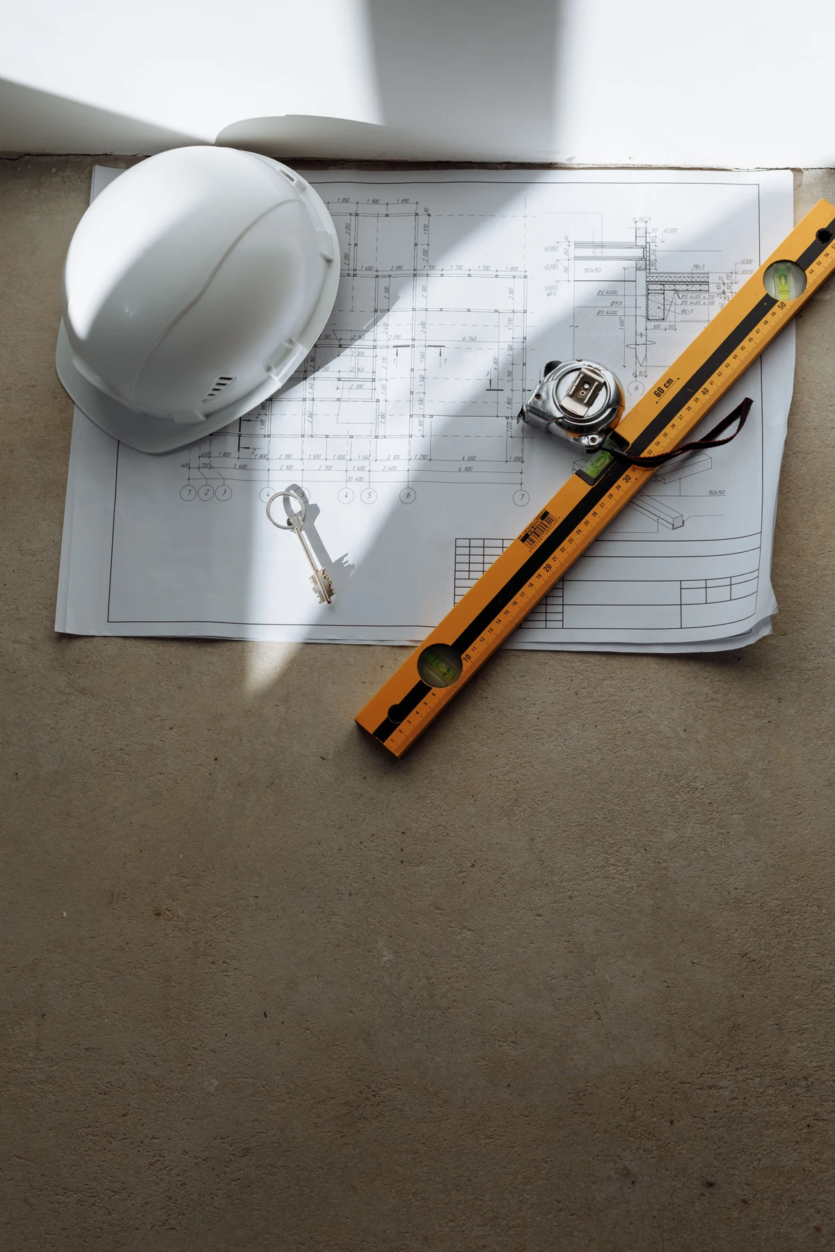 White safety helmet, measuring tools and a spirit level arranged over building plans