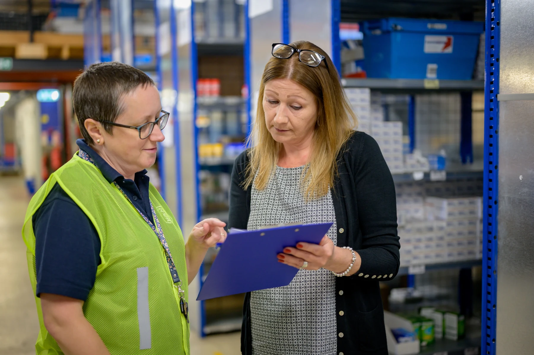 Two colleagues reviewing a clipboard in a warehouse, one wearing a high-visibility vest